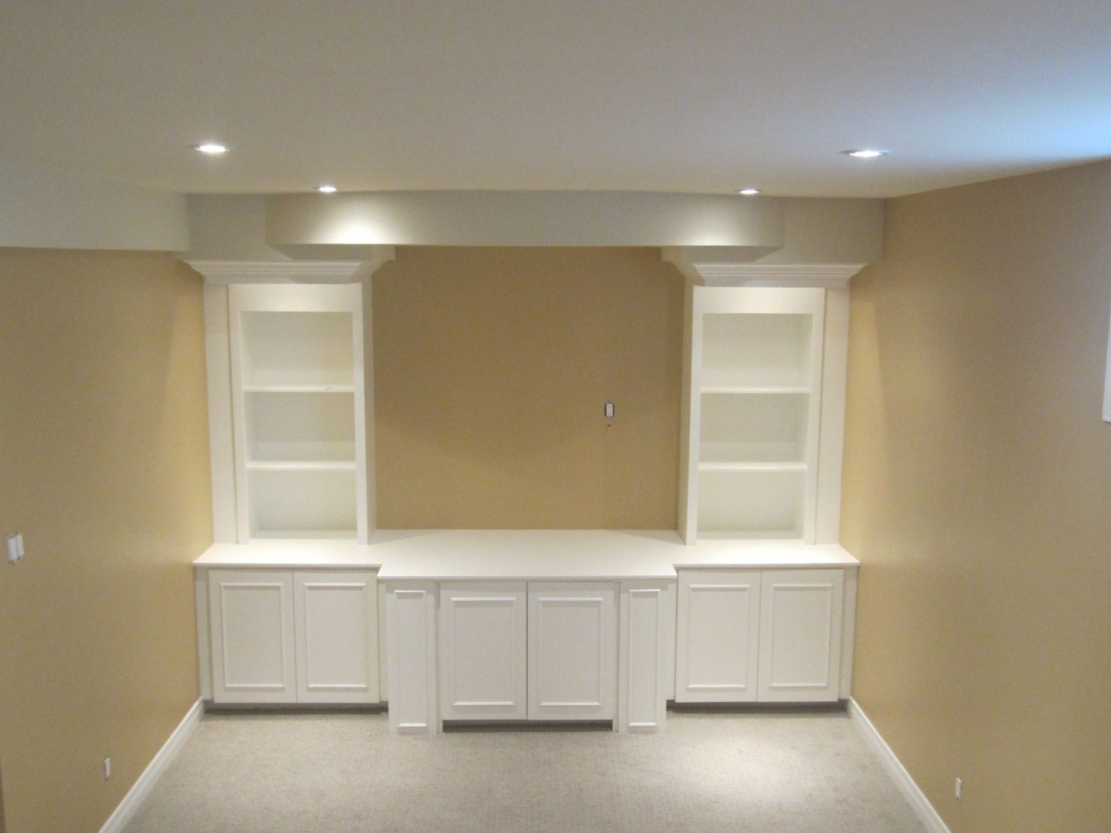 A finished basement media wall with an arched bulkhead, lit shelves and white base cabinets