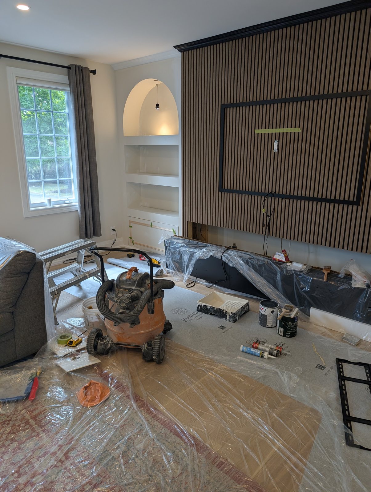 A slat feature wall with a black TV frame cut into it and a lit arched niche beside it, in Kanata
